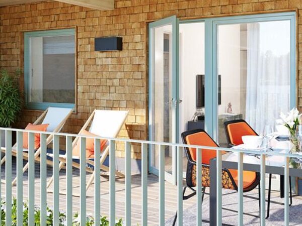 En balkongmiljö med träfasad, öppna dörrar och sittplatser illustrerar de levande och funktionella boendemiljöer som GBJ Bygg skapar för att främja utomhusvistelse och vardaglig trivsel.