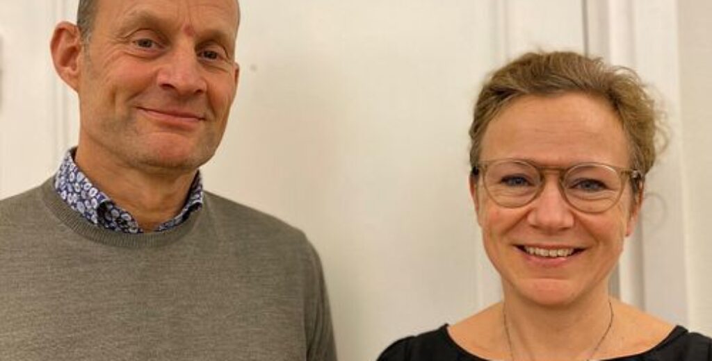 Två medarbetare poserar leende i en kontorsmiljö, vilket speglar GBJ Byggs professionella och engagerade arbetskultur där samarbetet mellan teamen är en central del av verksamheten.