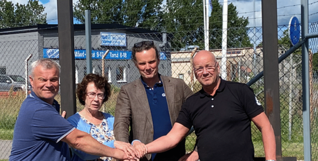 En grupp människor tar i hand vid en skylt och markerar starten på ett nytt projekt, där GBJ Bygg bidrar med expertis och genomförandekraft i kommande byggprocess.