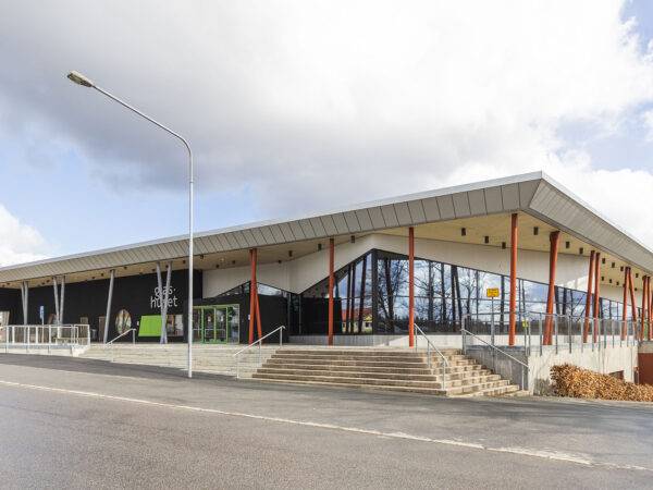 En modern byggnad med framträdande glasfasader och långt utskjutande tak visas från gatan; byggnaden, uppförd av GBJ Bygg, skapar ett öppet och välkomnande uttryck som passar Glashusets publika funktion.