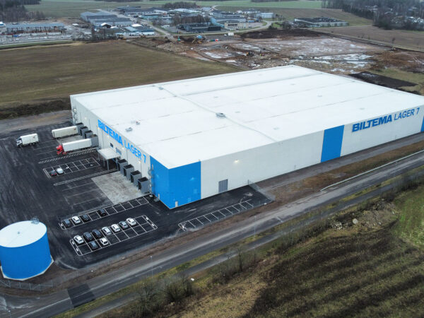 Flygbild över Biltemas omfattande lagerkomplex visar en modern distributionsanläggning med tekniska installationer och stora hårdgjorda ytor där GBJ Bygg skapat en robust och kapacitetsstark logistikhubb för framtida expansion.