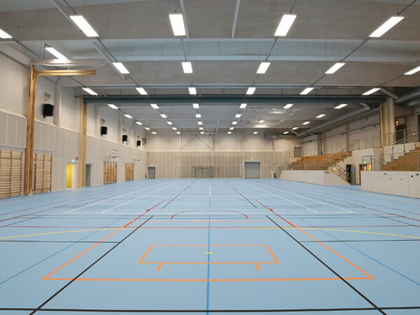 En sporthall med linjer för olika aktiviteter och högt i tak visar GBJ Byggs arbete med att bygga hållbara och flexibla idrottsytor för skola och föreningsliv.