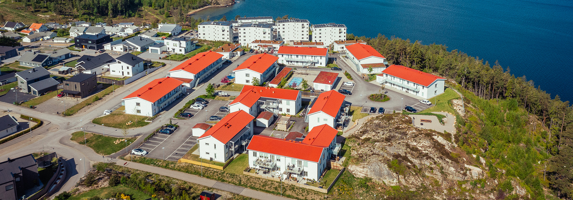 Flygbild över hela bostadsområdet visar en tydlig struktur av vita trähus med röda tak, där GBJ Bygg skapat ett sammanhängande och naturnära kvarter med utsikt över Uddevallas kustlinje.