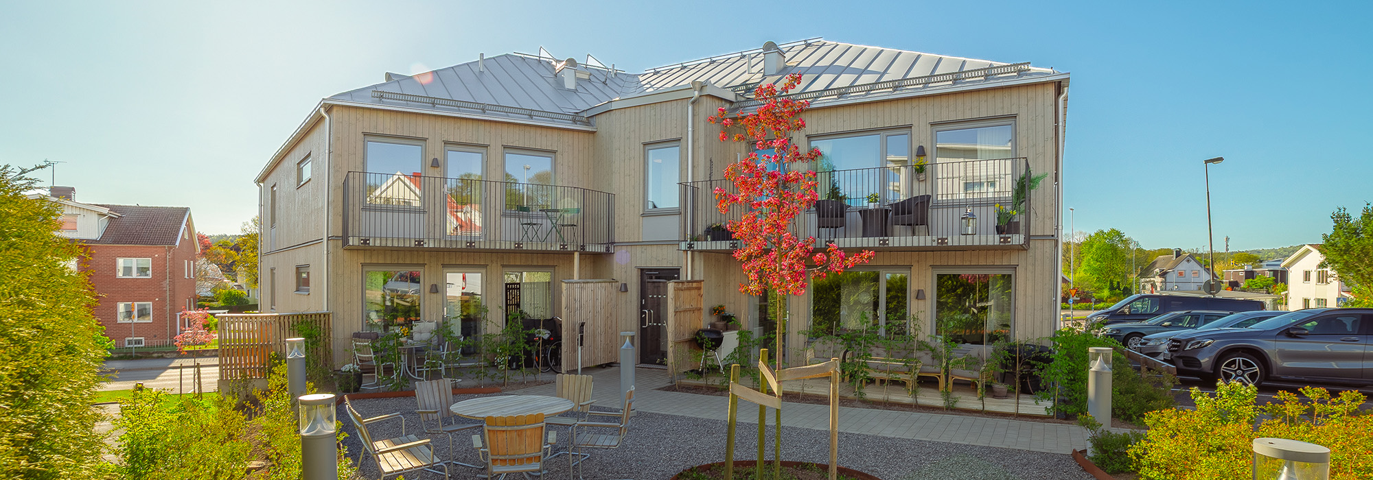 Vy mot innergården där stora fönster, balkonger och höstfärgade träd ger Lilla Apeln ett varmt uttryck; GBJ Bygg har skapat en social och estetiskt sammanhängande boendemiljö.