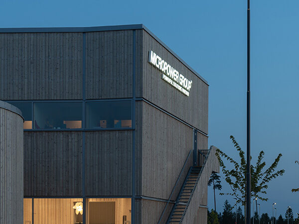 Fasadvyn i skymning framhäver träpanel, stora fönsterpartier och Micropowers logotyp; byggnaden, utförd av GBJ Bygg, signalerar teknisk innovation genom sitt moderna uttryck.