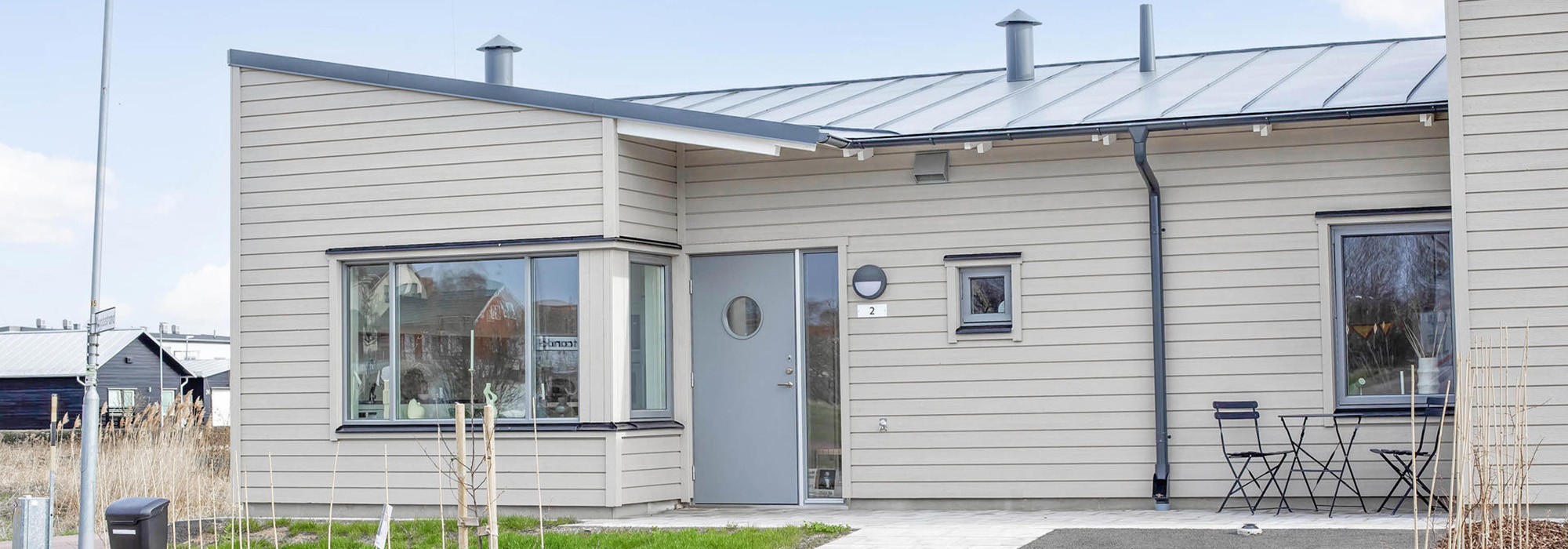 En bredare vy av samma bostadstyp där en stilren träbyggnad, uppförd av GBJ Bygg, framträder med sina låga taklutningar, stora fönsterpartier och en trivsam uteplats som speglar företagets fokus på välplanerade och hållbara boendemiljöer.