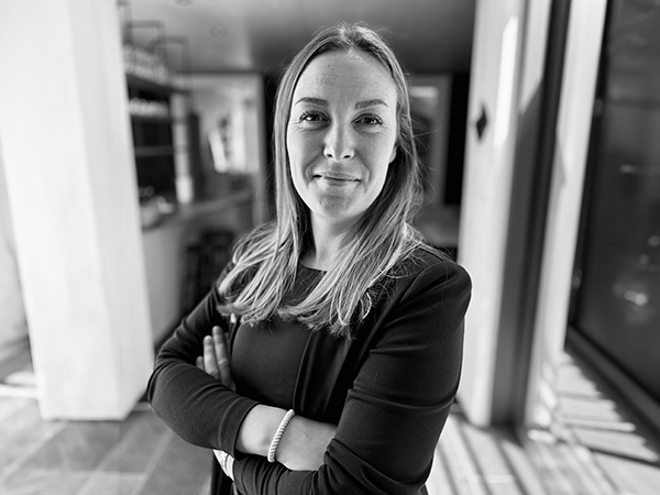 Entreprenadingenjör Linnea Hansson från GBJ Bygg står med armarna i kors och möter kameran med ett vänligt leende i en modern kontorsmiljö. Porträttet lyfter företagets medarbetare och förmedlar kompetens, professionalism och engagemang i bygg- och entreprenadverksamheten.