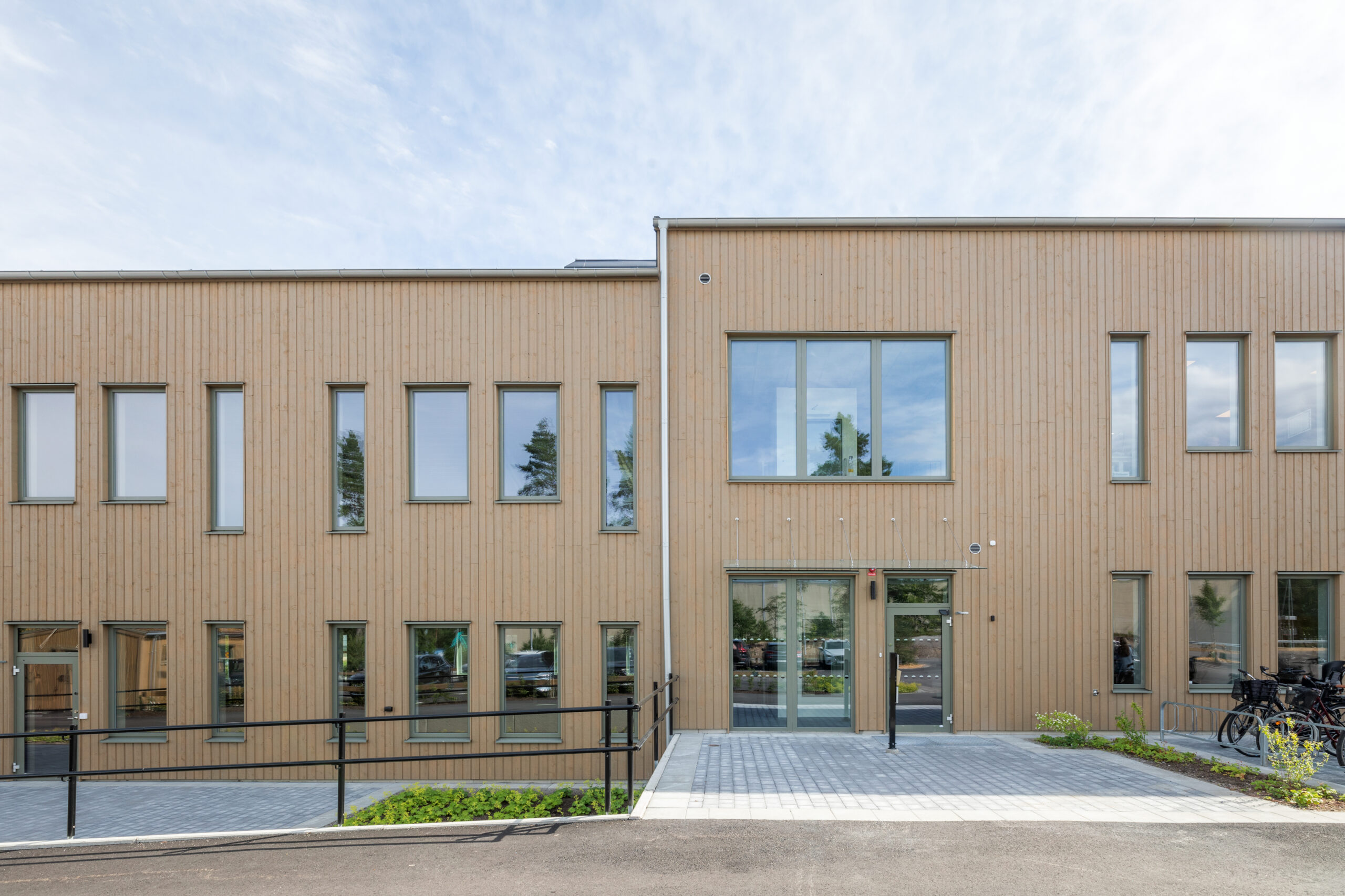 En modern träklädd byggnad i Växjö med varierade fönsterpartier, glasad entré och tillgänglig gångväg. GBJ Bygg står bakom byggprojektet, där den ljusa träfasaden ger byggnaden ett varmt och samtida uttryck.