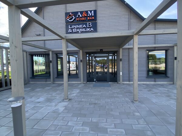En entré till en verksamhetsbyggnad ramas in av en träpergola och ljus träfasad, med stenlagd gångyta framför. GBJ Byggs utförande skapar ett välkomnande uttryck med naturliga material och tydligt markerad entré.