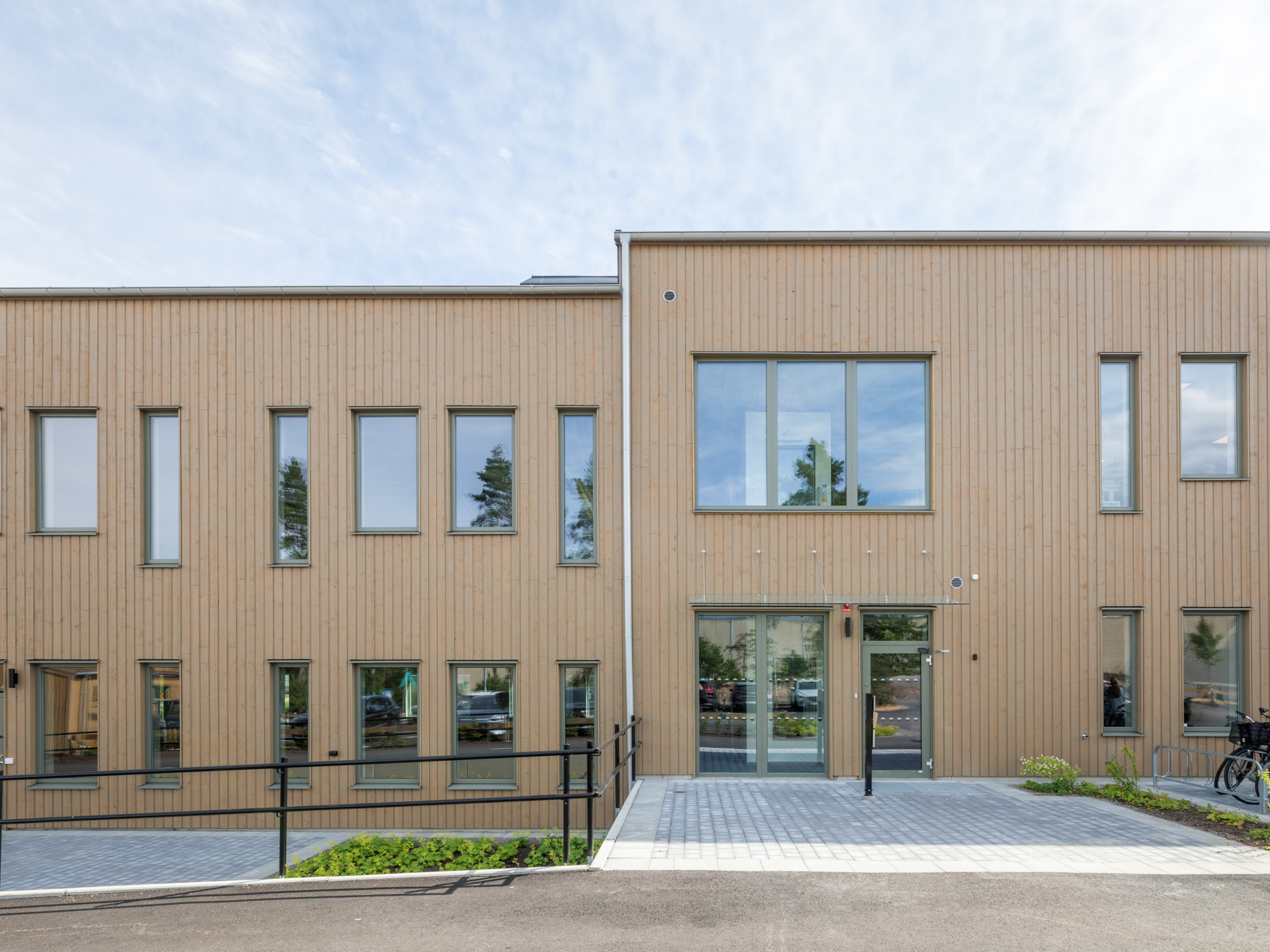 En modern träklädd byggnad i Växjö med varierade fönsterpartier, glasad entré och tillgänglig gångväg. GBJ Bygg står bakom byggprojektet, där den ljusa träfasaden ger byggnaden ett varmt och samtida uttryck.